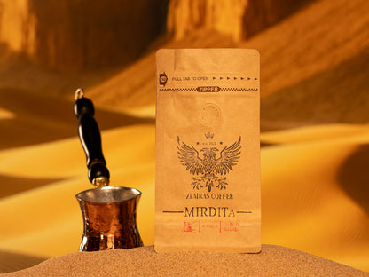Premium Mirdita Turkish grind coffee bag resting on sand next to a traditional handcrafted copper xhezve.
