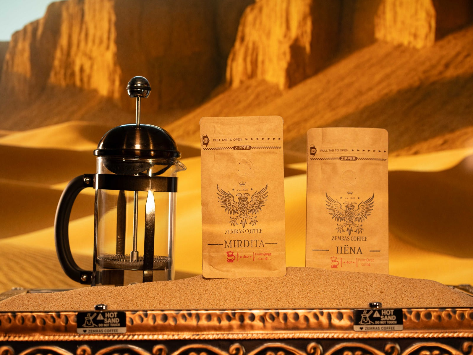 Mirdita and Hëna specialty coffee bags with a French press on a sand-brewing station, roasted in Charlotte by Enderly Coffee.